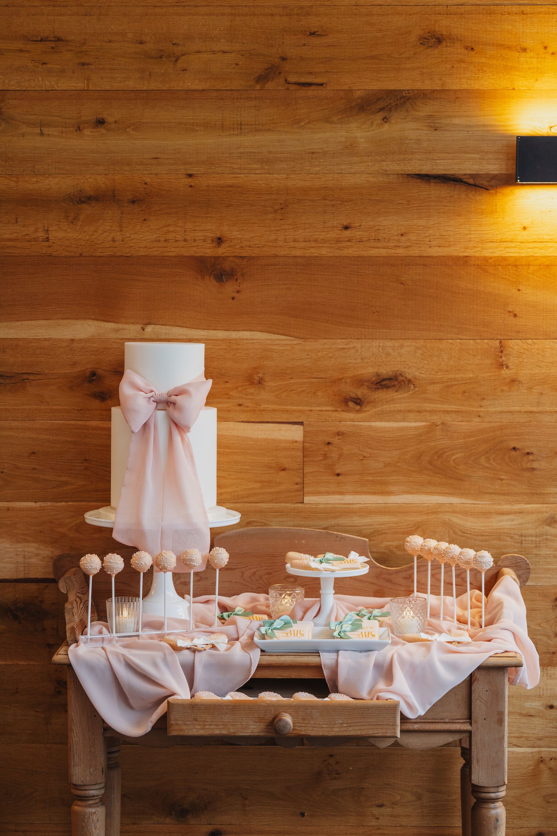 Elegant dessert table with blush decorations and cake pops against a wooden wall