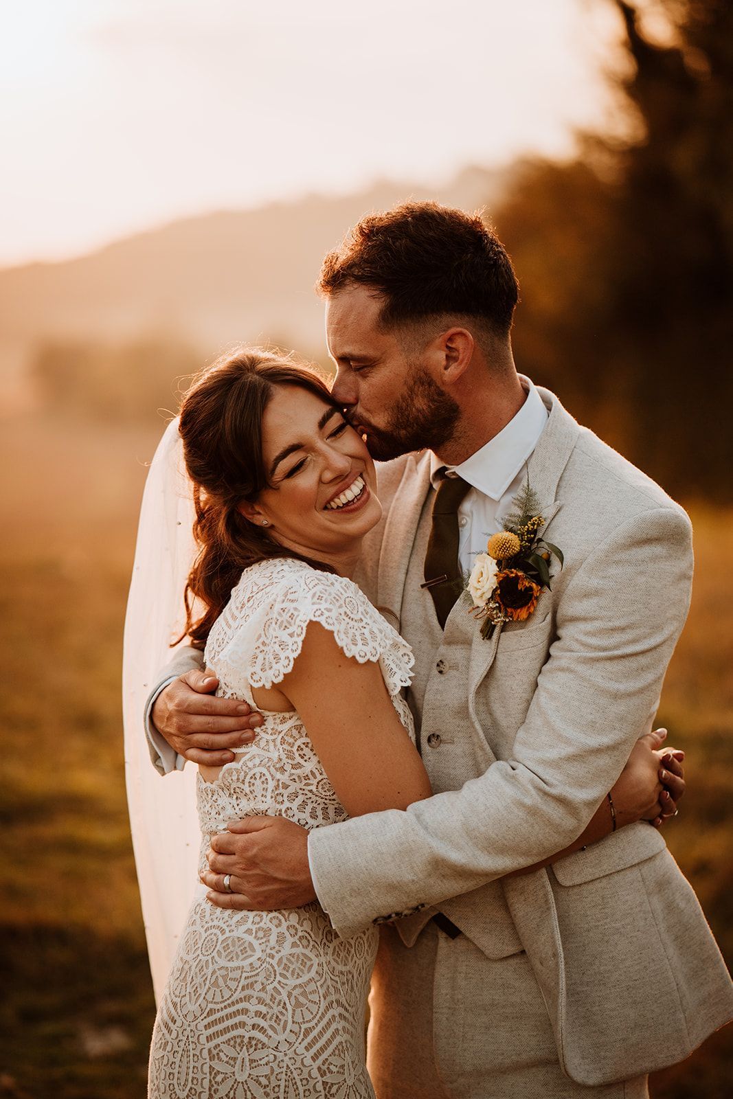 Couple embracing in a sunlit stone archway, with the bride in a lace gown and veil.