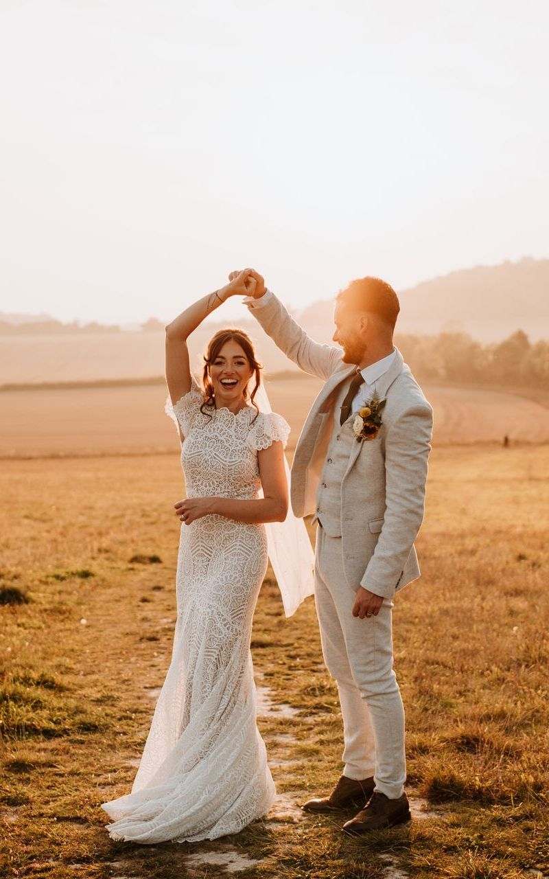 Couple dancing outdoors in a sunlit field, the woman in a white lace dress and the man in a light suit.