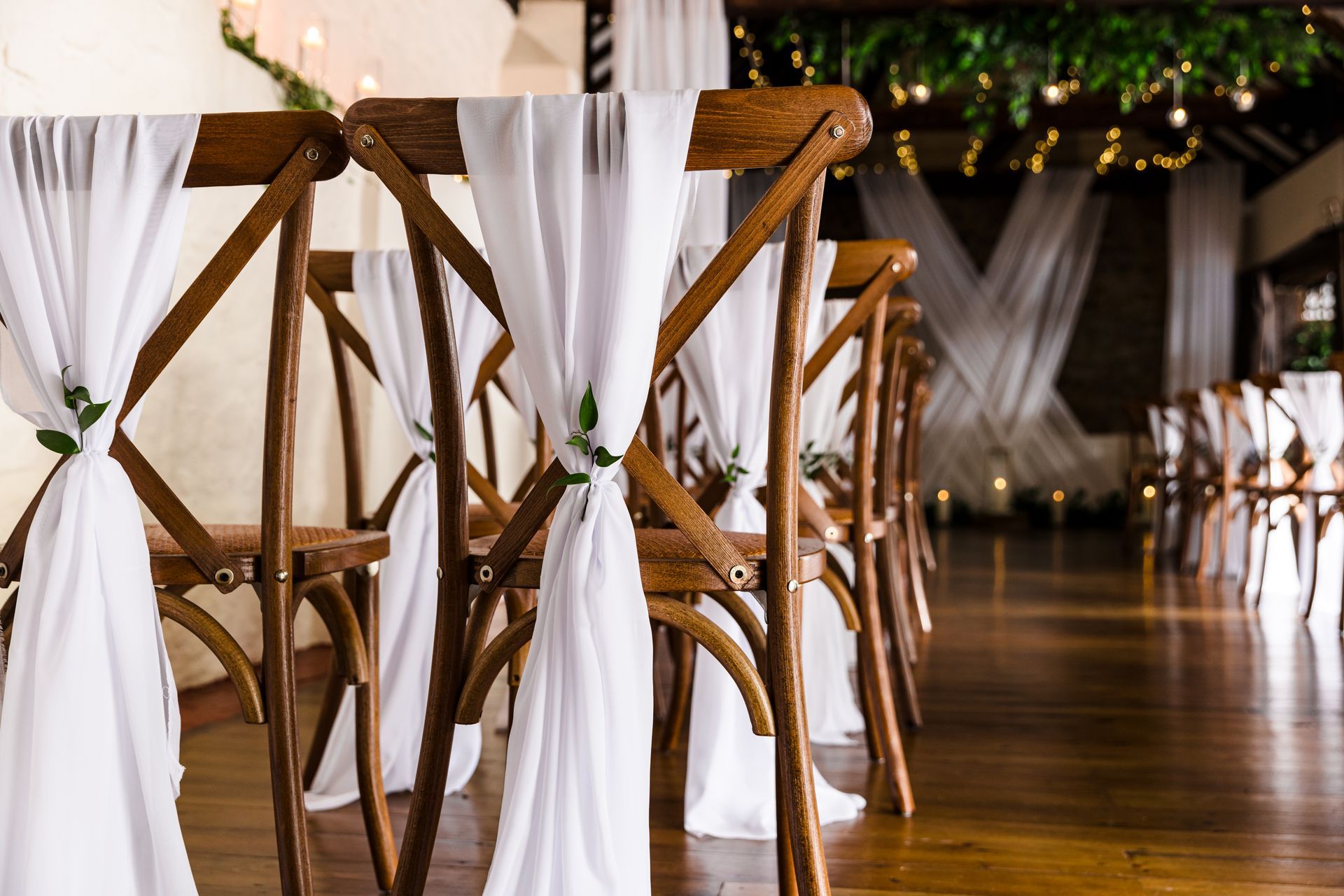 White-draped wooden chairs arranged along a polished aisle in a warmly lit event venue