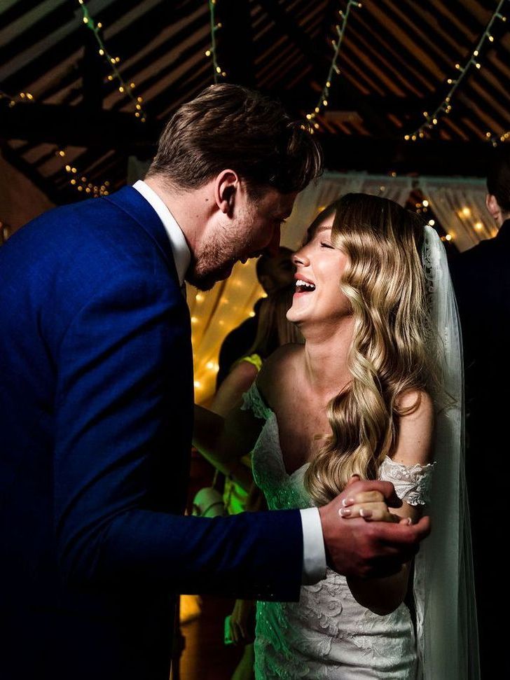Couple dancing and smiling at a warmly lit party, with string lights in the background.