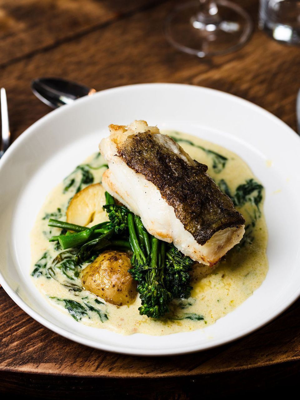 Plated fish over creamy green sauce with asparagus on a white dish at a restaurant table