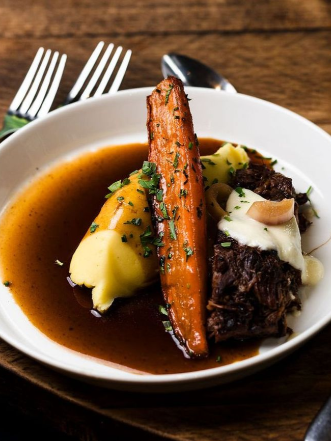 Plated meat with carrots, mashed potatoes, and dark gravy on a white dish