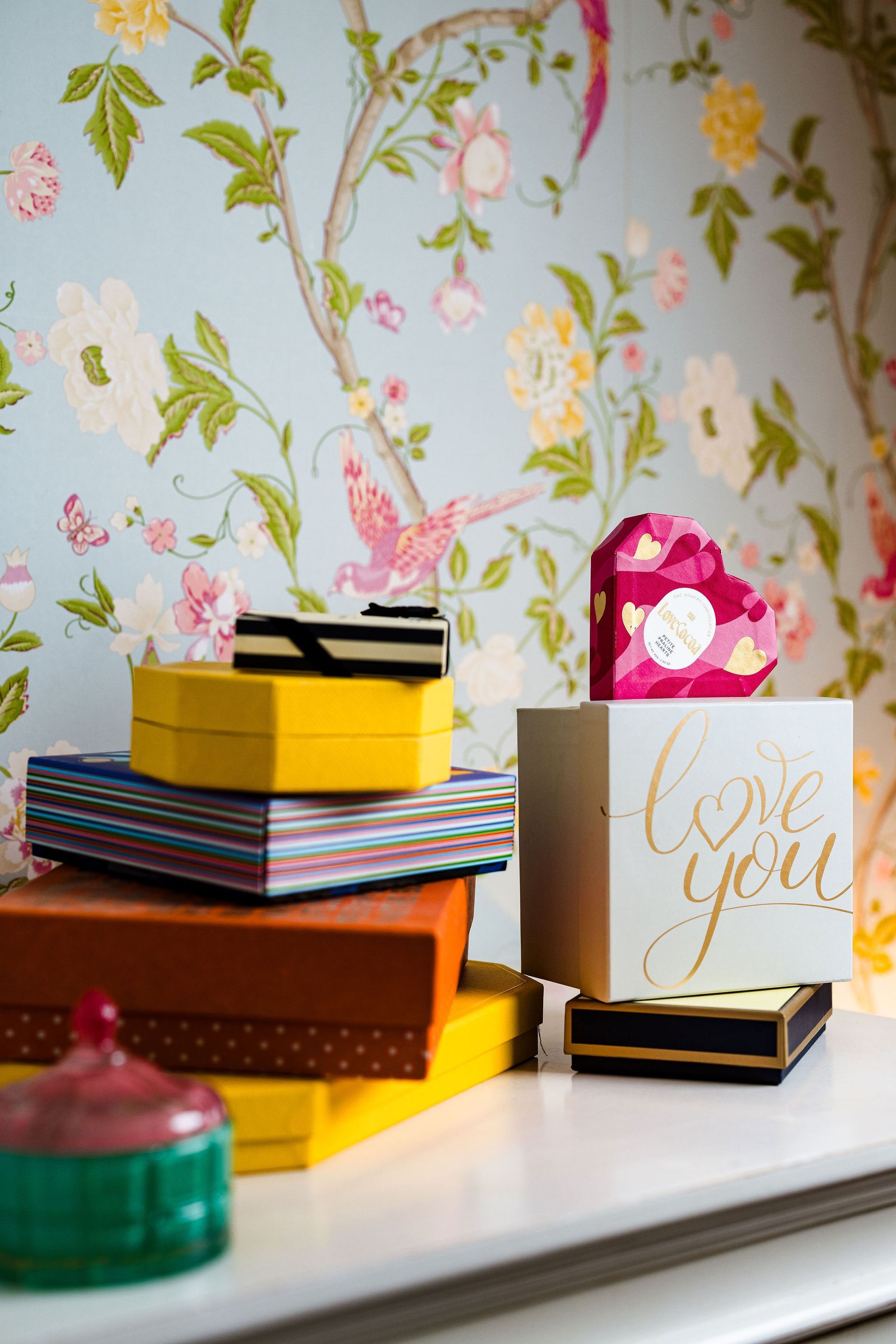 Colorful gift boxes stacked on a windowsill beside floral wallpaper and a white card reading “love you”