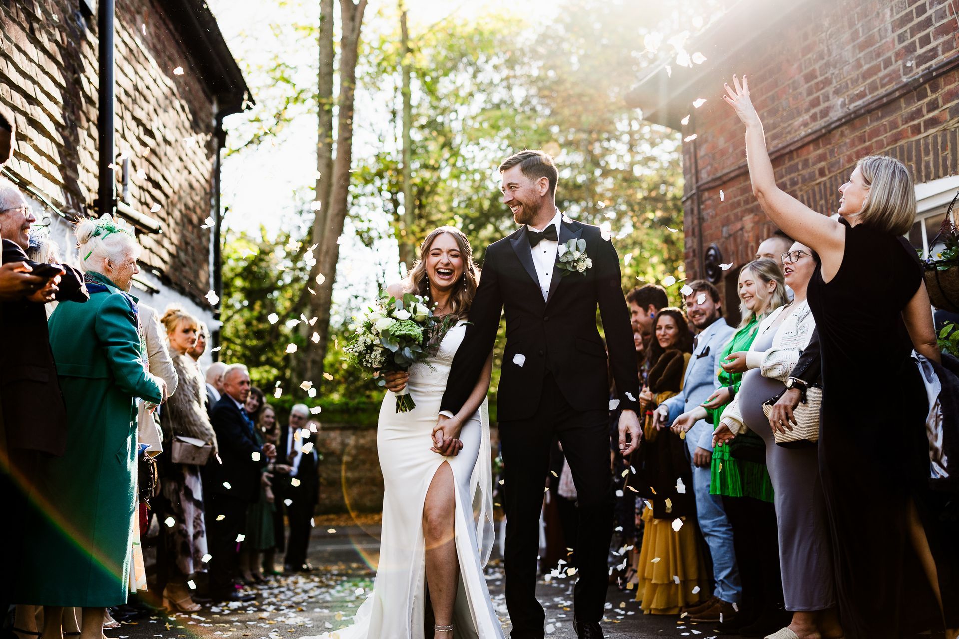 Wedding couple walking down an outdoor aisle as guests applaud in a sunlit courtyard