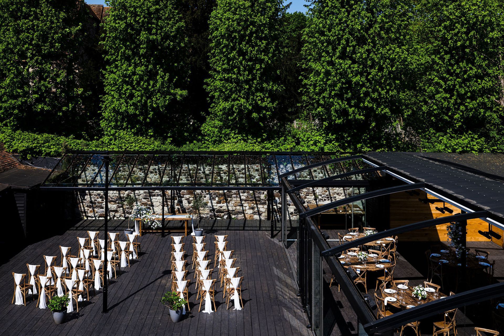 Rows of lit candles on a dark terrace beside a hedge-lined garden