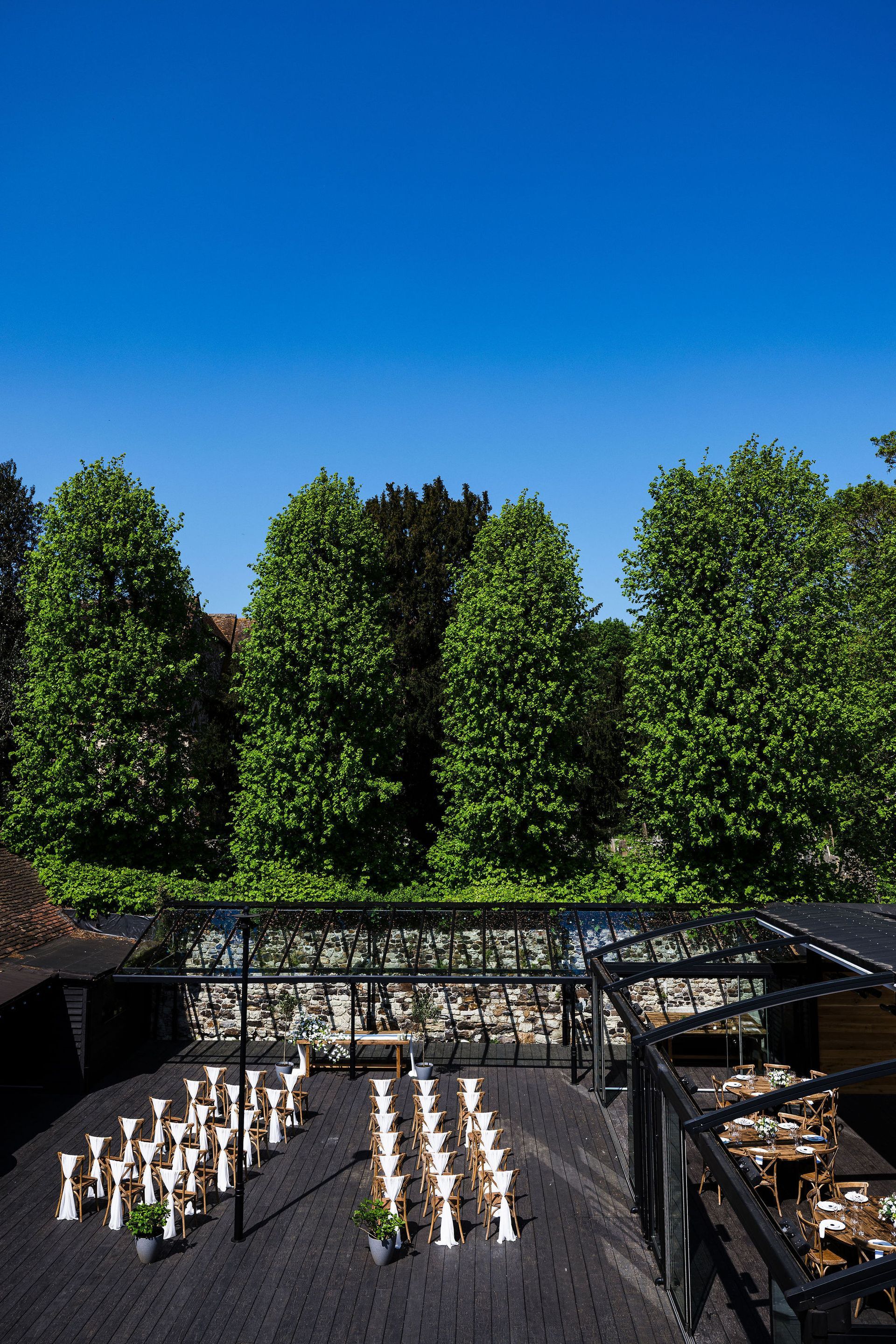 Outdoor memorial with rows of white candles beneath a black canopy and tall green trees under a blue sky