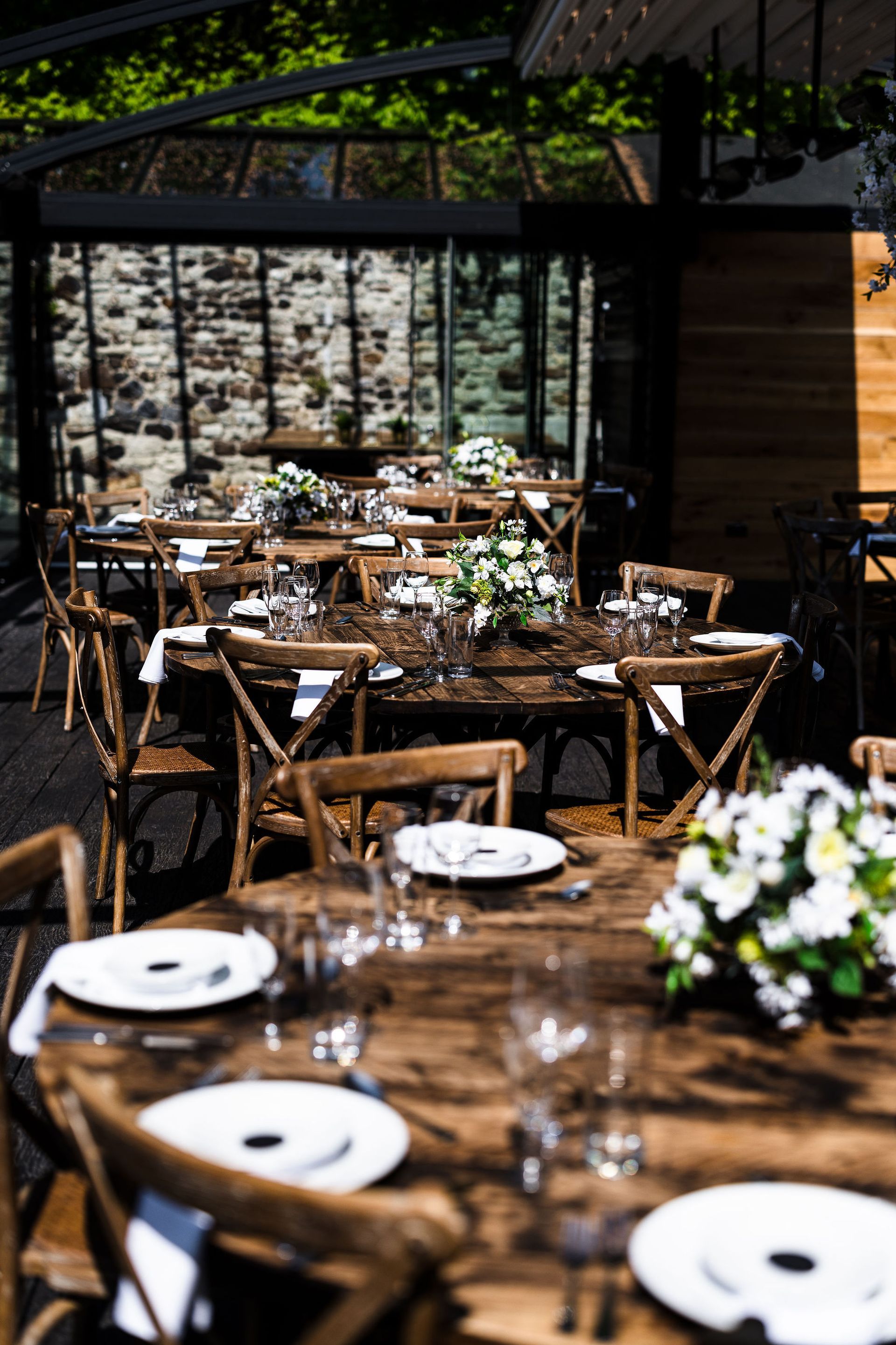 Rustic outdoor dining setup with wooden tables, white plates, and glasses in a garden setting