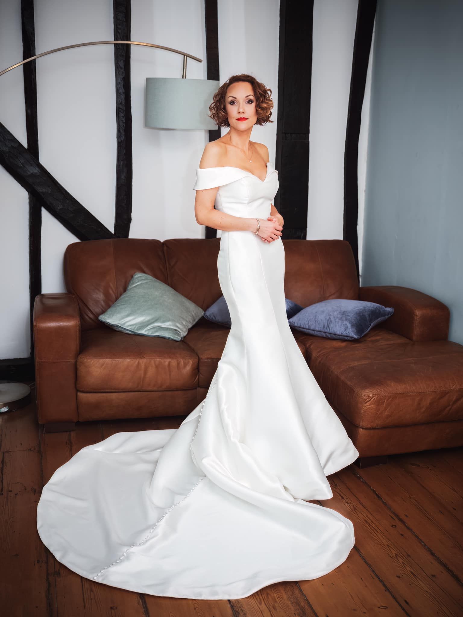 Woman in a white gown posing on a brown leather sofa in a living room.