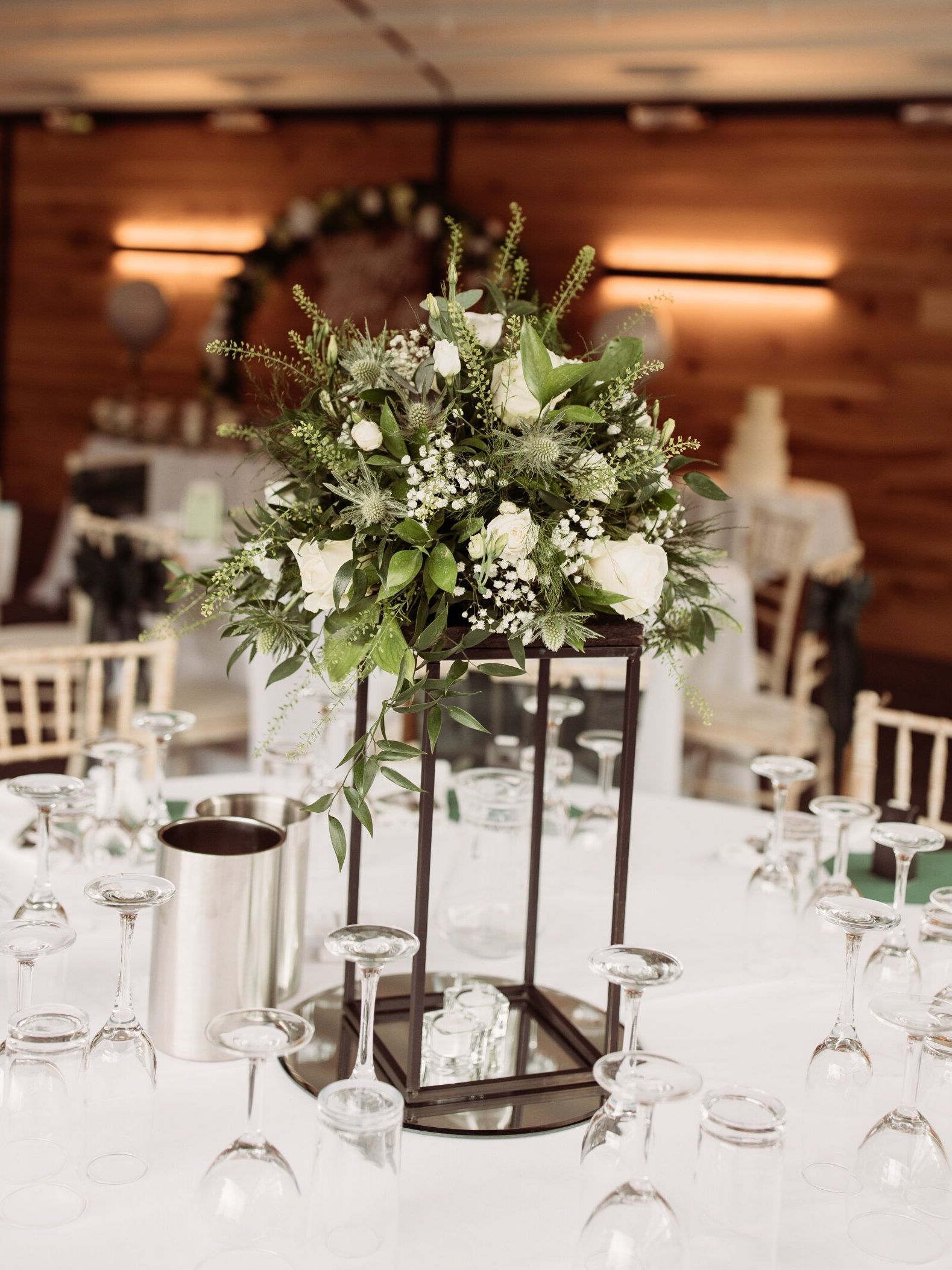 Floral centerpiece with white flowers and greenery on a formal dining table in a wood-paneled venue