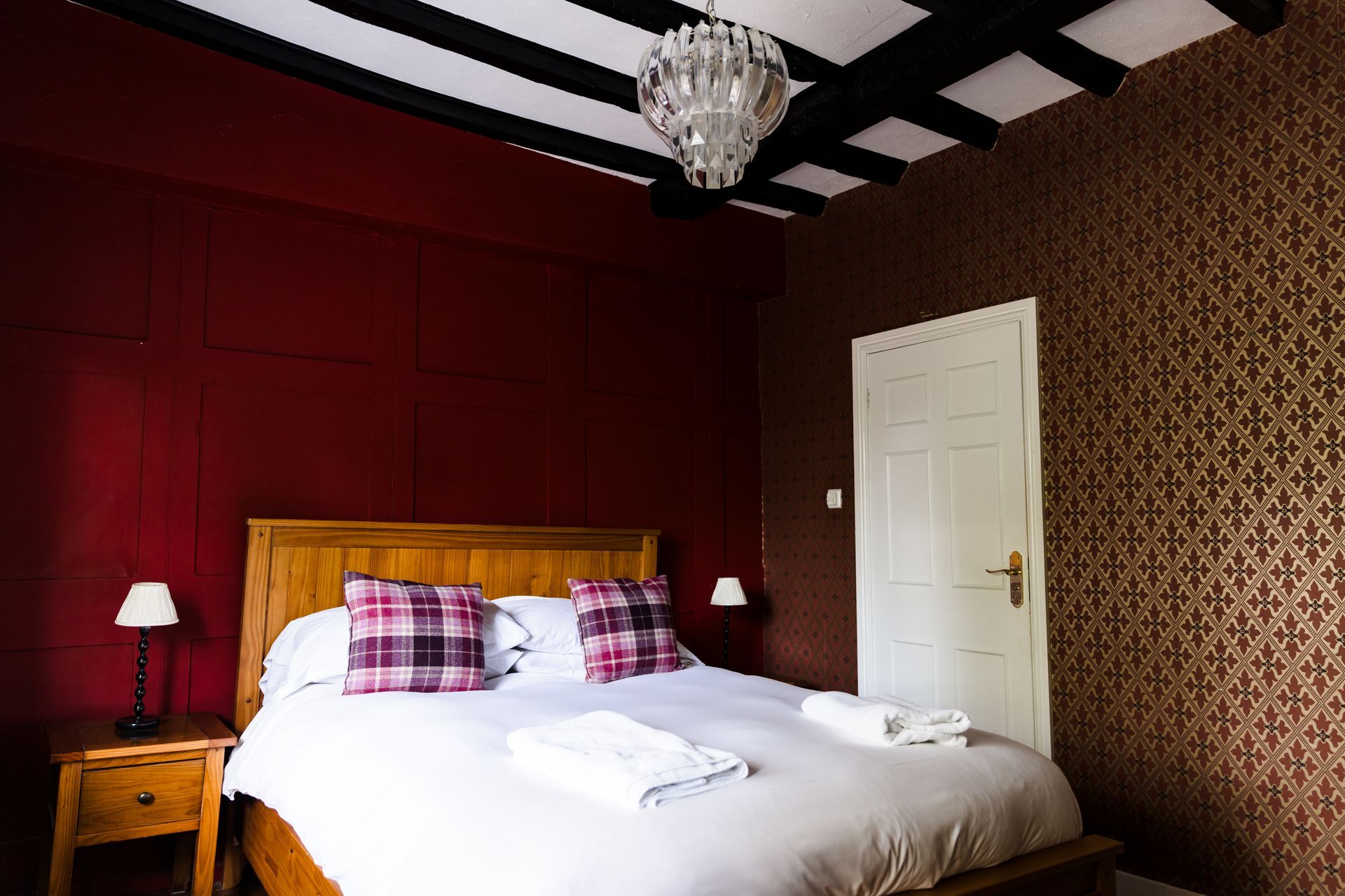 Bedroom with a wooden bed, white bedding, red walls, patterned wallpaper, and a chandelier。