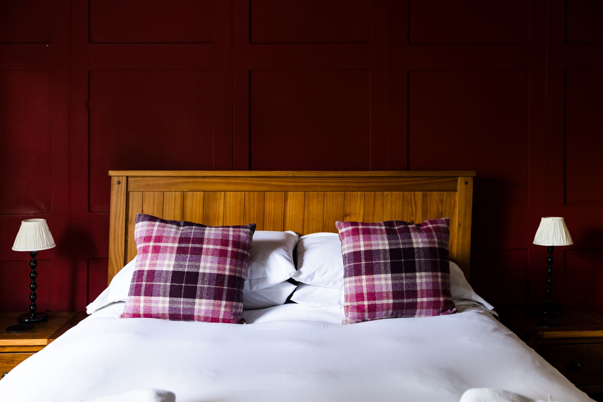 Double bed with white bedding and two plaid pillows against a dark red wall