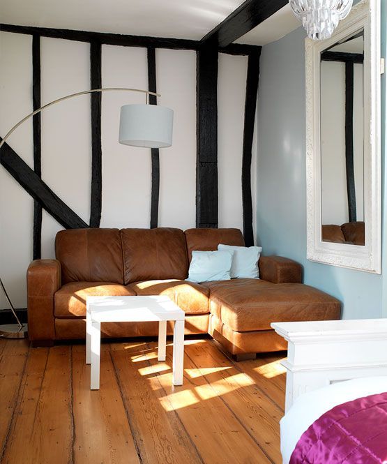 Cozy living room with brown leather sofa, white coffee table, striped walls, and wooden floor in sunlight