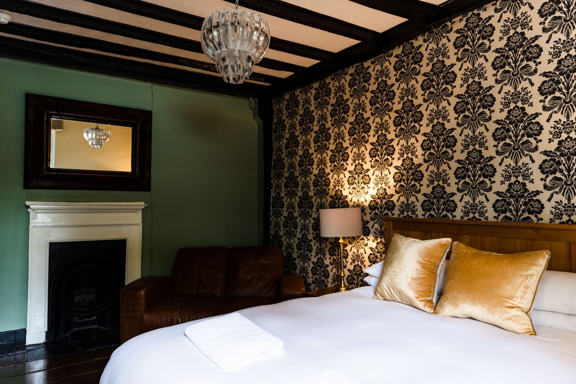 Stylish bedroom with dark floral wallpaper, green walls, white bed, and fireplace