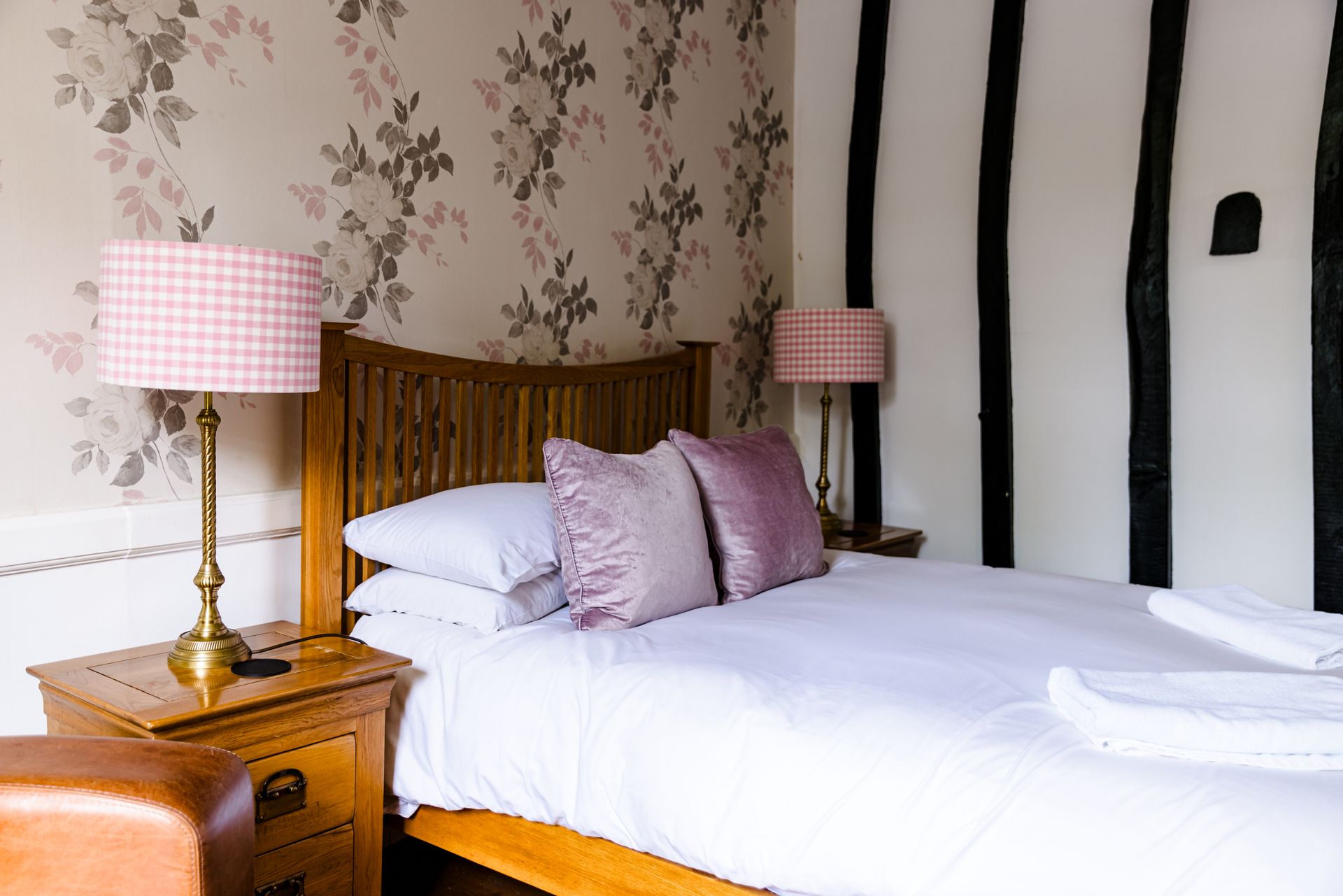 Cozy bedroom with white bed, pink lamps, floral wallpaper, and black-and-white striped accent wall
