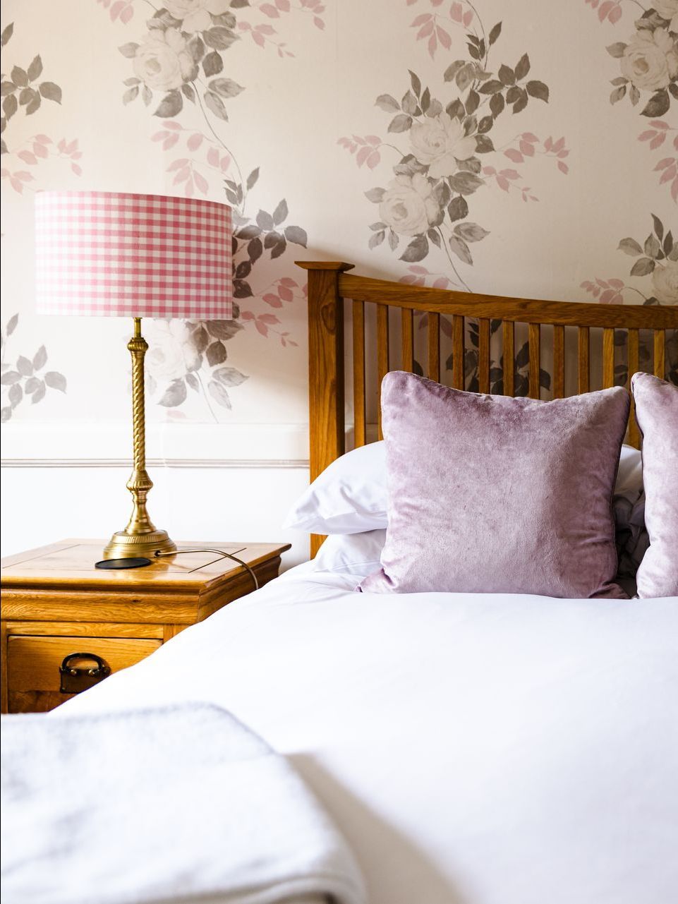 Cozy bedroom with wooden bed, pink lamp, floral wallpaper, and white bedding