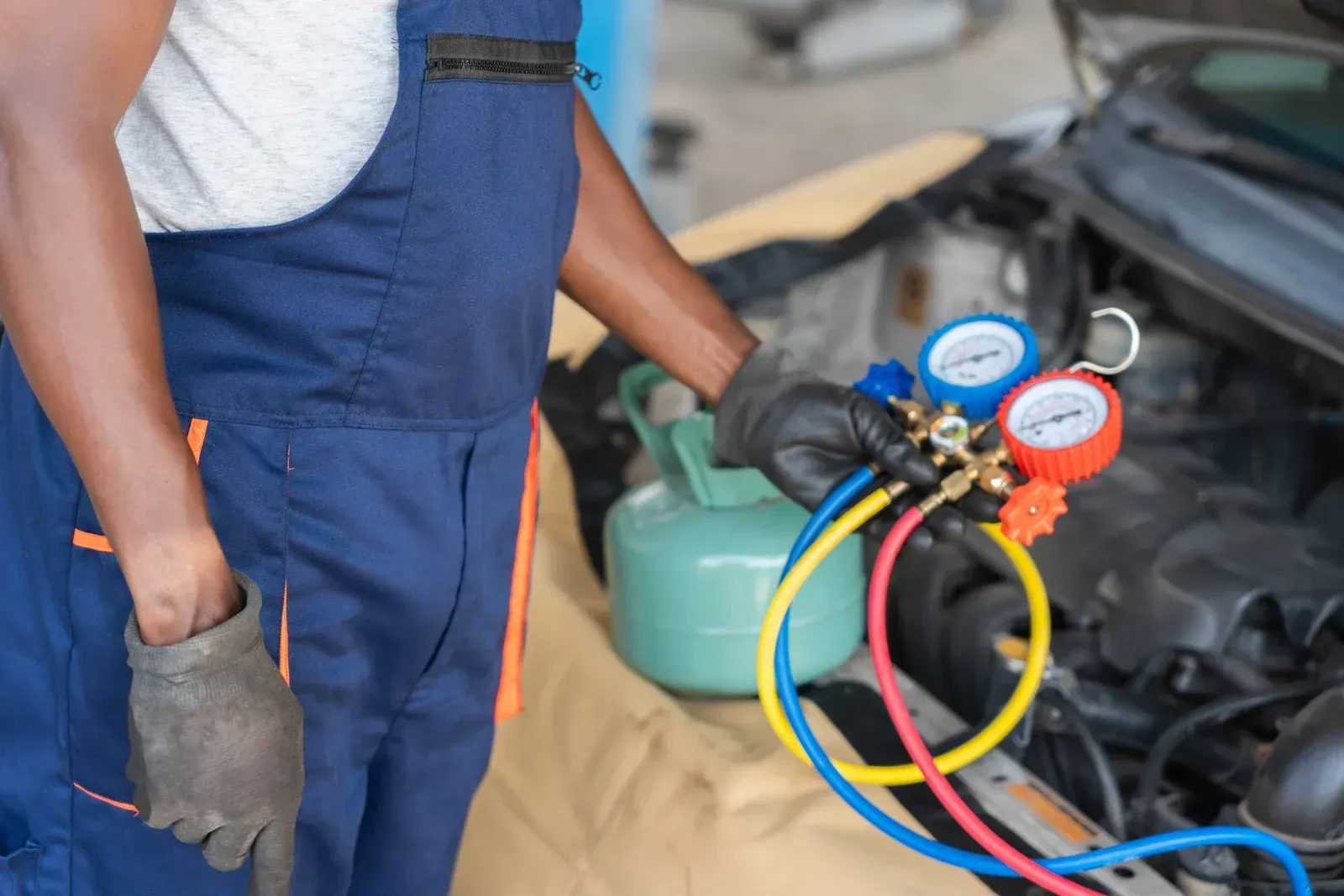 Mechanic in blue overalls uses gauges to service a car's AC unit.
