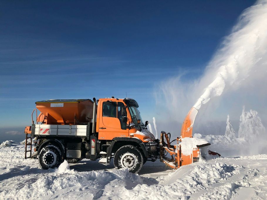 Orange snowplow clearing snow with a high spray of snow in a snowy landscape