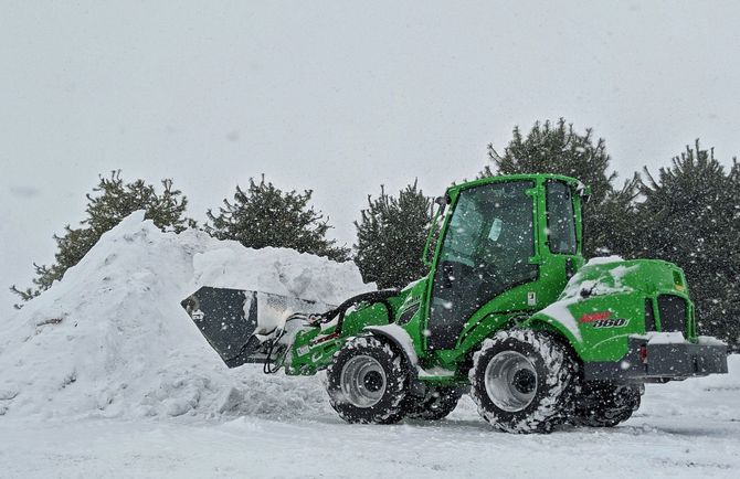 Green loader clearing a large snow pile on a snowy road