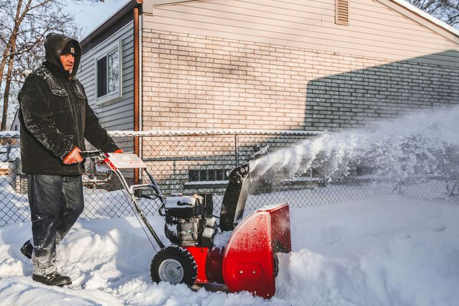 Person using a snow blower to clear snow beside a house in winter