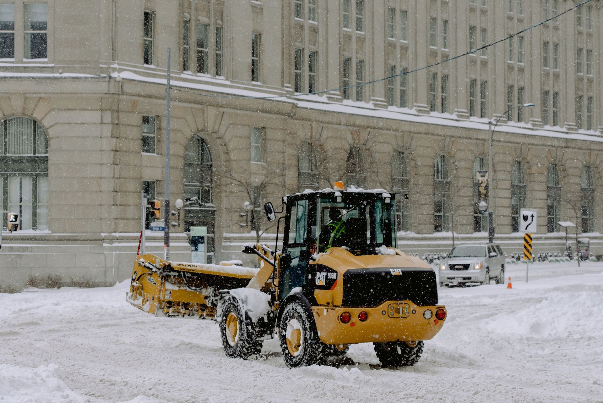 Yellow snowplow clearing snow in front of a large building during winter