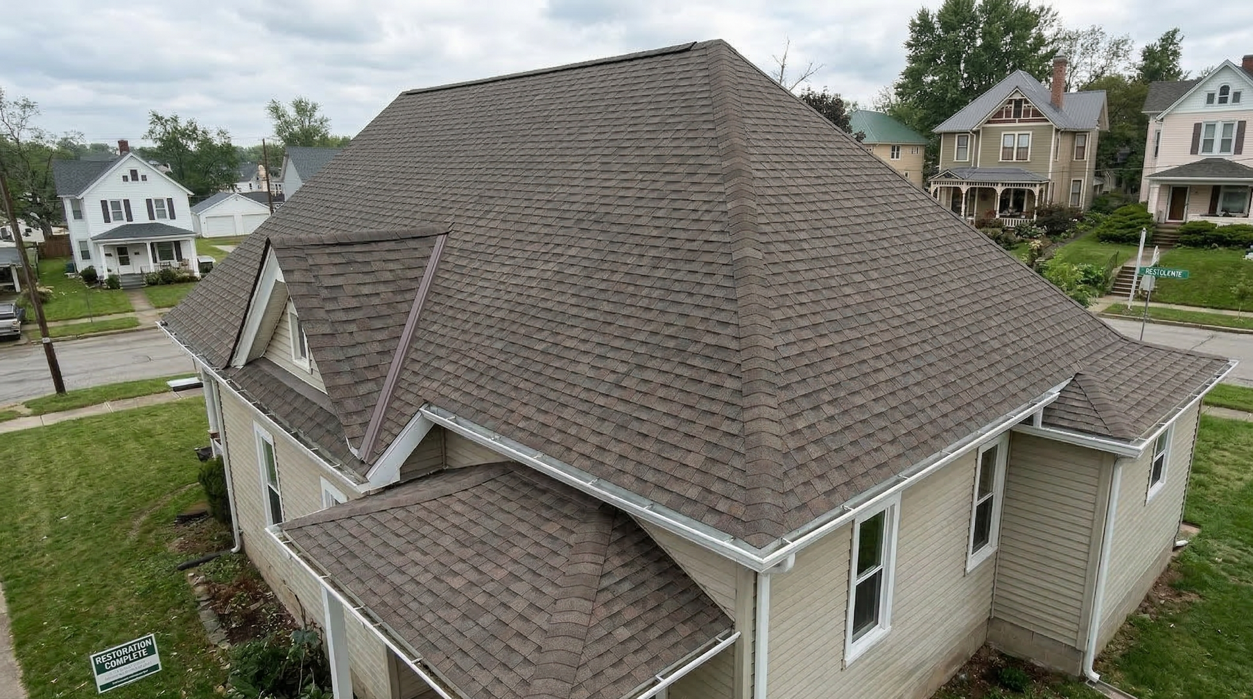 An aerial view of a tan-colored house with a new brown shingled roof, set in a residential neighborhood.