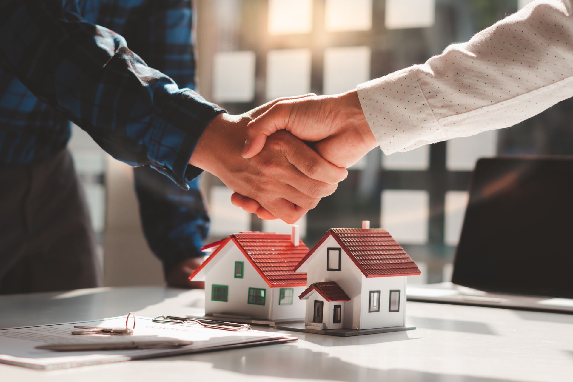 Two people shaking hands over a table with two miniature house models and paperwork. Two people shaking hands over a table with two miniature house models and paperwork.
