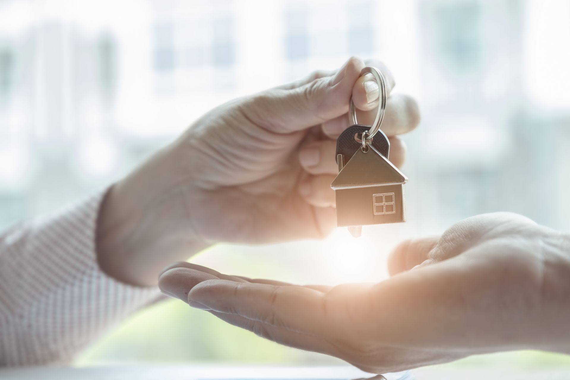 Hands exchanging house keys with a house-shaped keychain, symbolizing a real estate transaction.