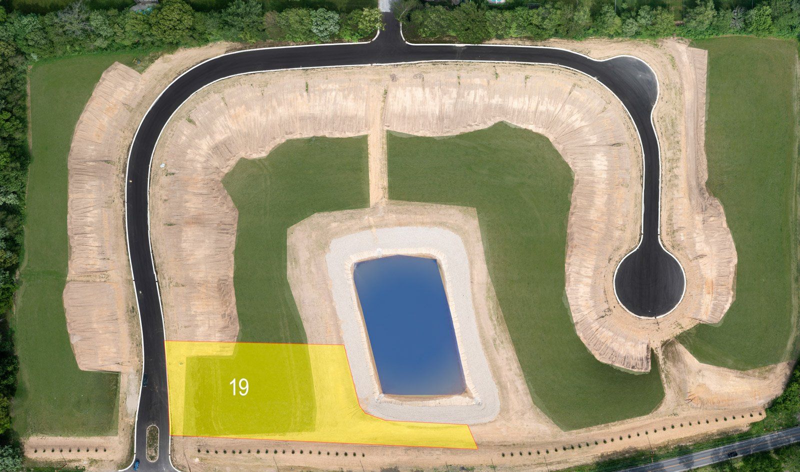 Aerial view of a construction site with roads, a pond, and a highlighted lot (19) in yellow.