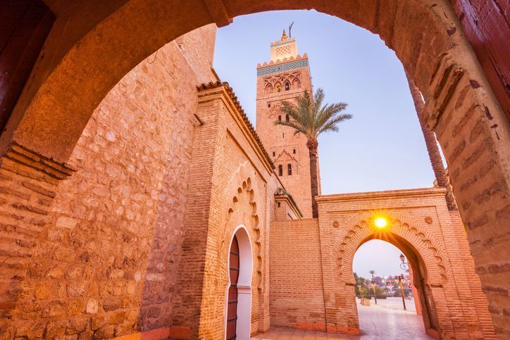 Archi in mattoni incorniciano la vista del minareto della moschea Koutoubia a Marrakech, in Marocco, sotto un cielo azzurro.