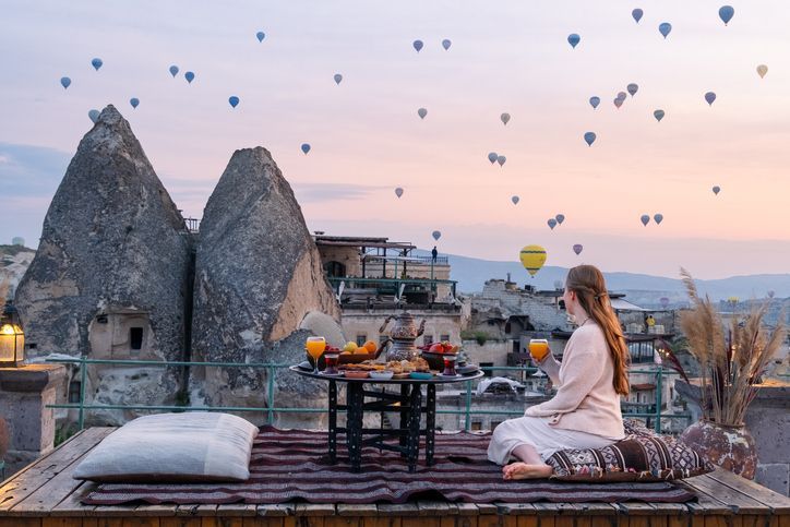 Donna che fa colazione su un tetto in Cappadocia, ammirando le mongolfiere all'alba.
