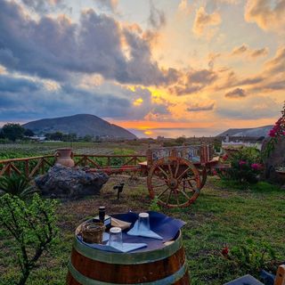 Vista del tramonto da un tavolo in un vigneto. Sullo sfondo un carro di legno, montagne e oceano.