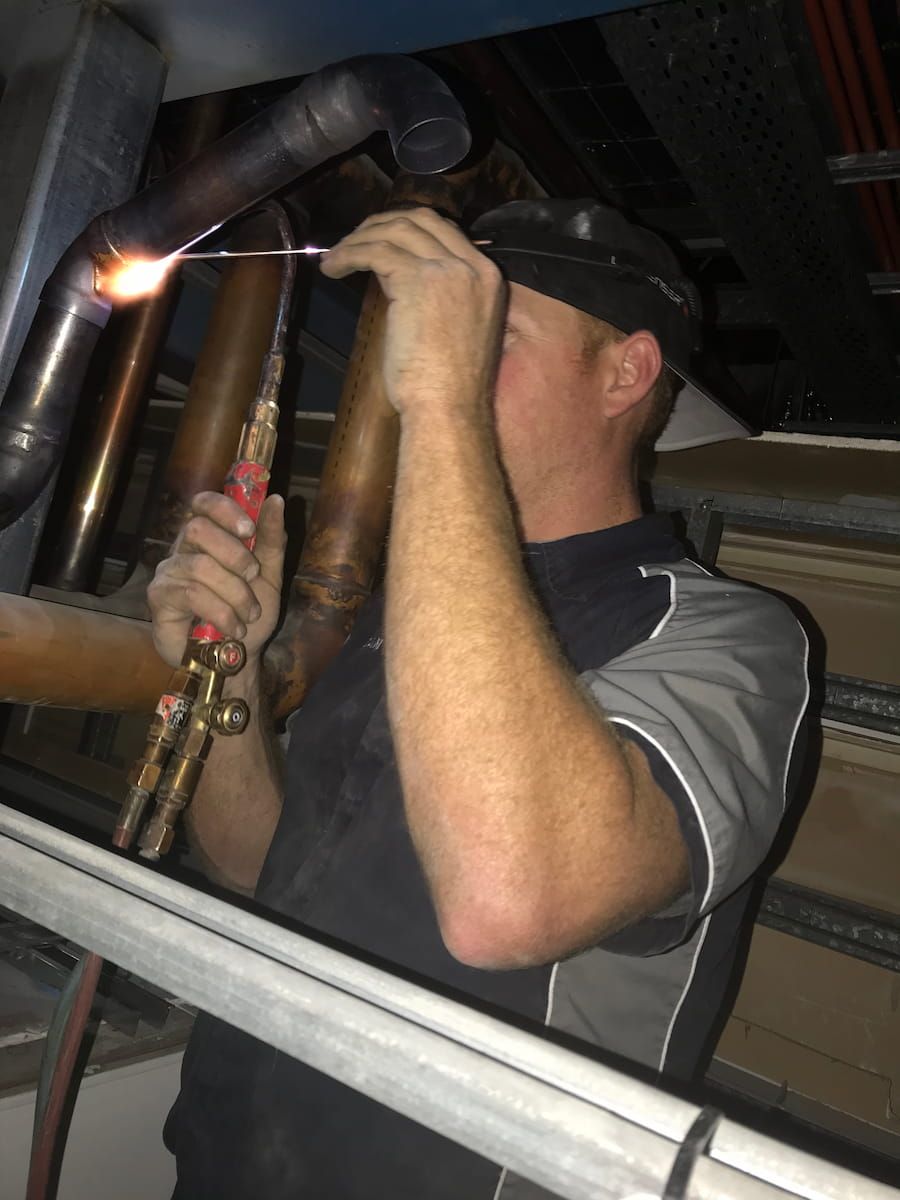 A Man Is Welding A Pipe With A Torch — Plumbmasters In Burleigh Heads, QLD