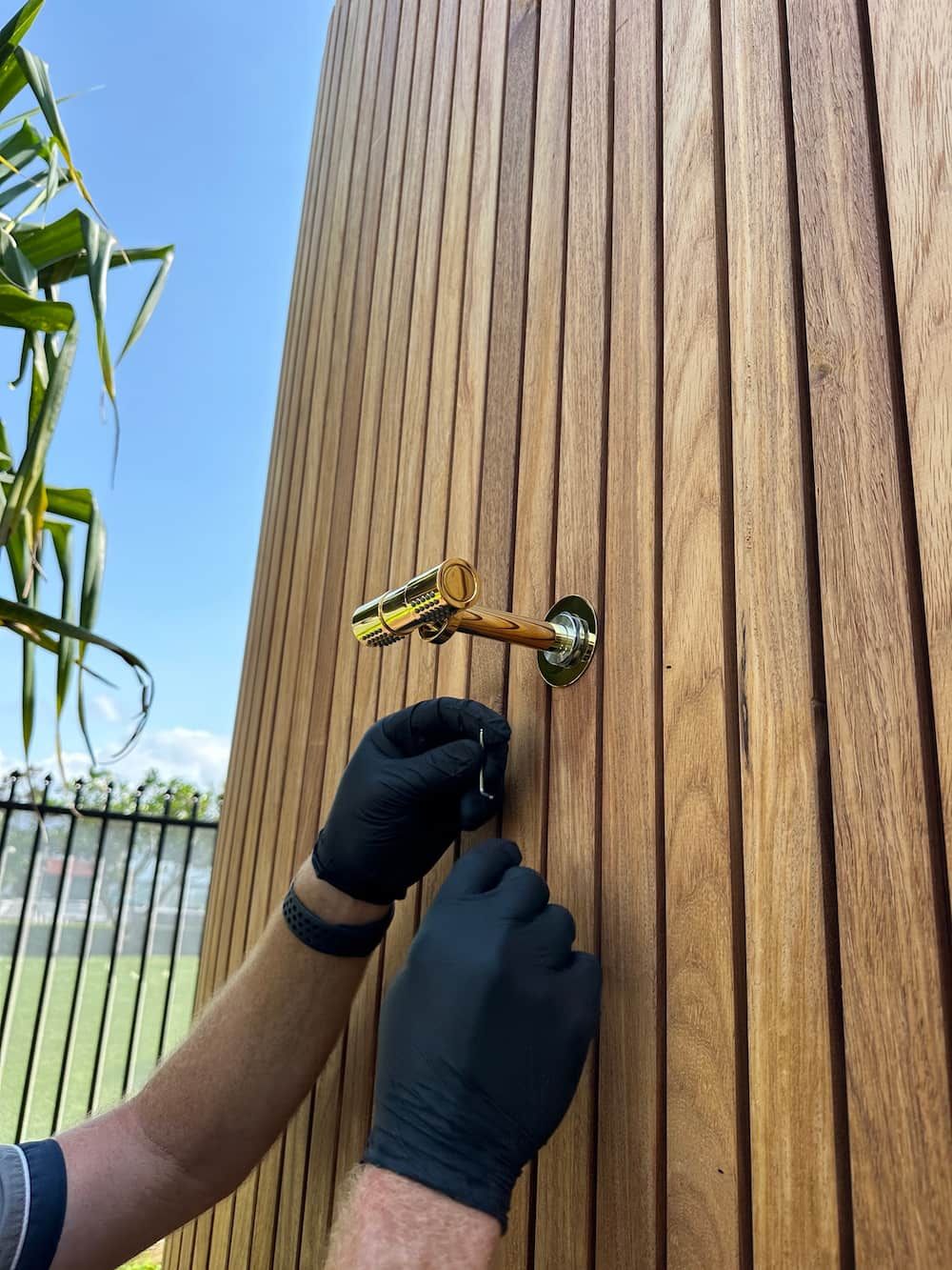 A Person Wearing Black Gloves Is Holding A Key On A Wooden Wall — Plumbmasters In Broadbeach, QLD