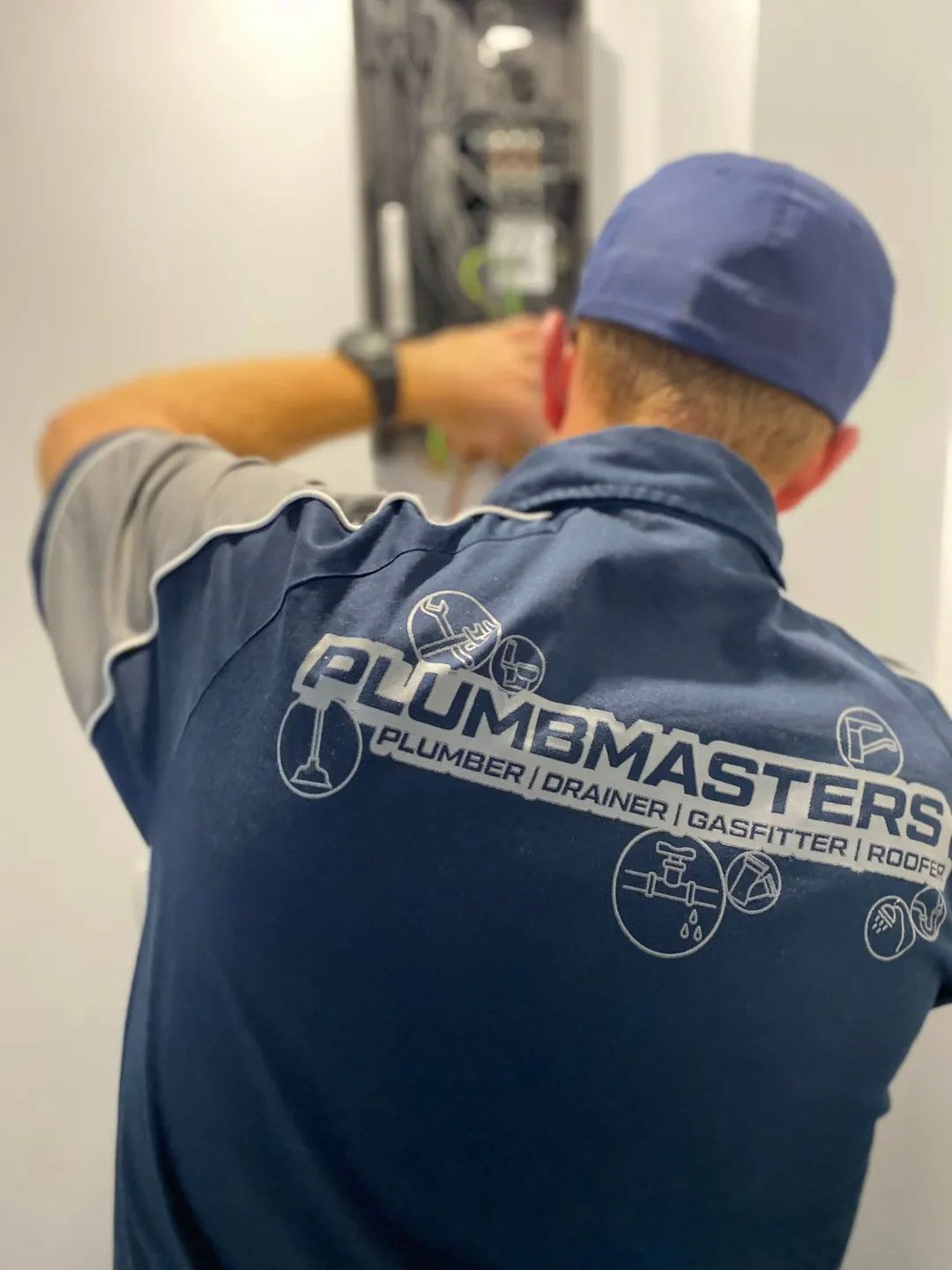 A Man Wearing A Plumbmasters Shirt Is Working On A Machine — Plumbmasters In Burleigh Heads, QLD