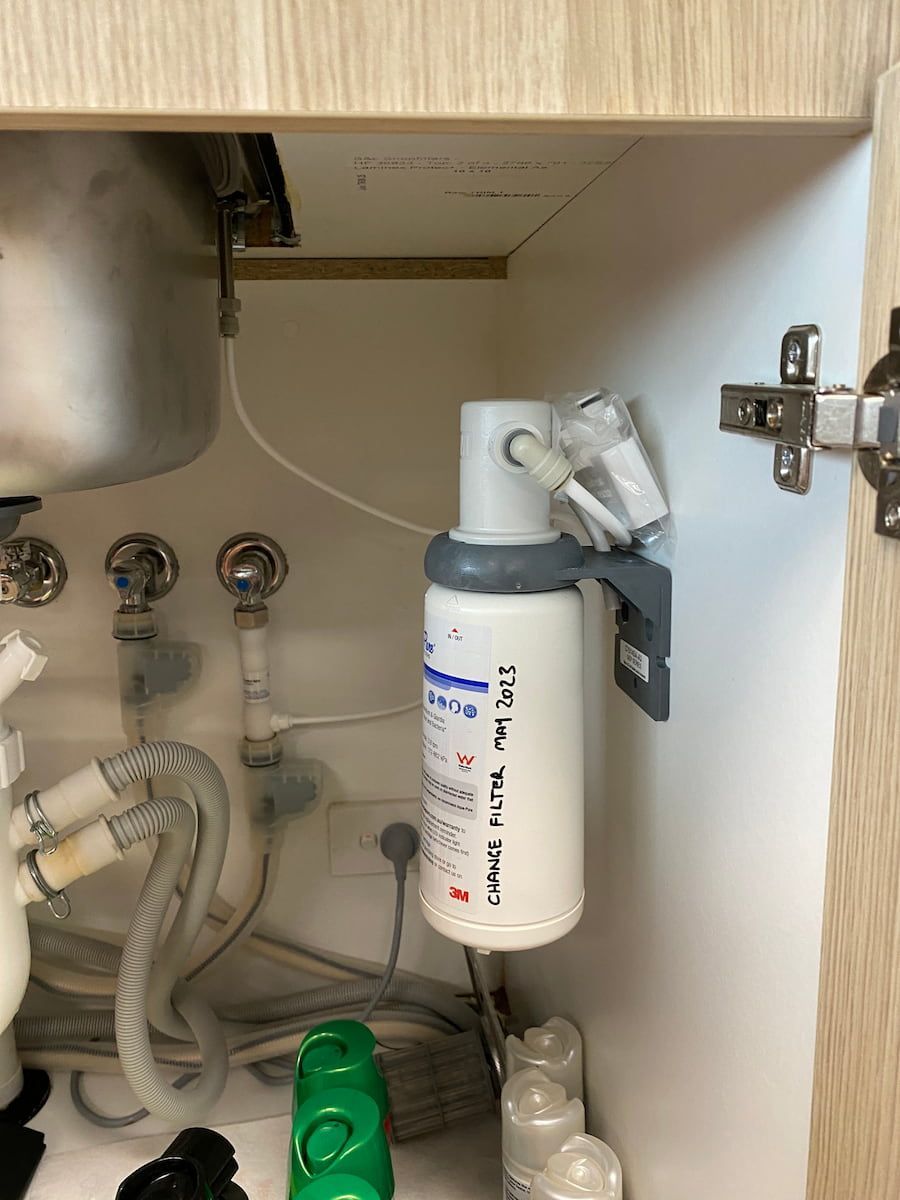 A Water Filter Is Hanging Under A Sink In A Cabinet — Plumbmasters In Burleigh Heads, QLD