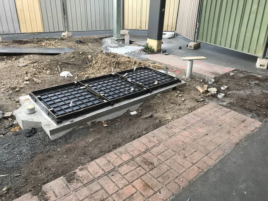 A Manhole Cover Is Sitting In The Dirt Next To A Brick Walkway — Plumbmasters In Palm Beach, QLD