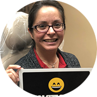 A woman wearing glasses is holding a laptop with a smiley face on it.