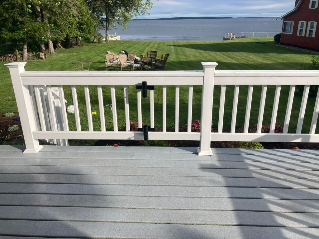 Wooden deck overlooking a grassy yard and lake, with white railing and red house on the right.