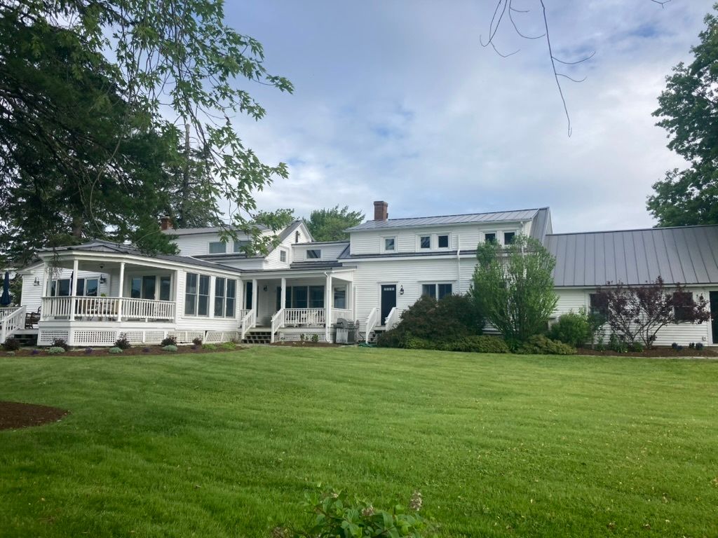 White house with screened porch and large green lawn under a partly cloudy sky