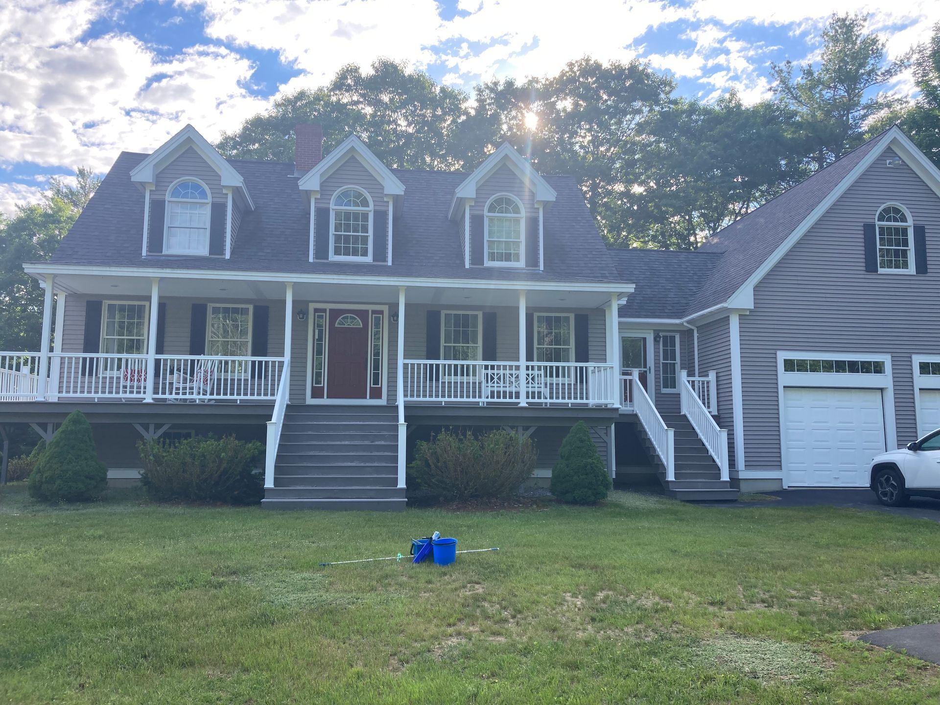 Large gray suburban house with white porch railings, front steps, driveway, and a parked white truck