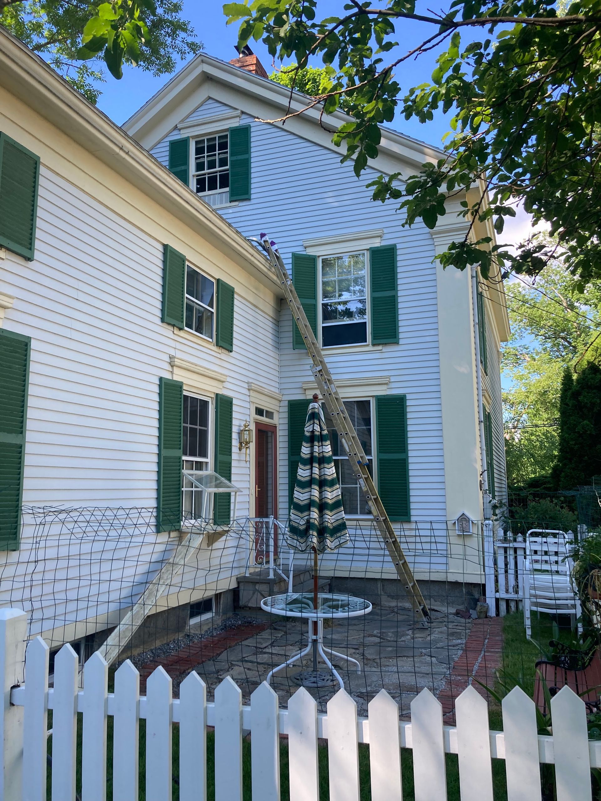 Hand spraying a rooftop gutter with a pressure washer beside a house and walkway