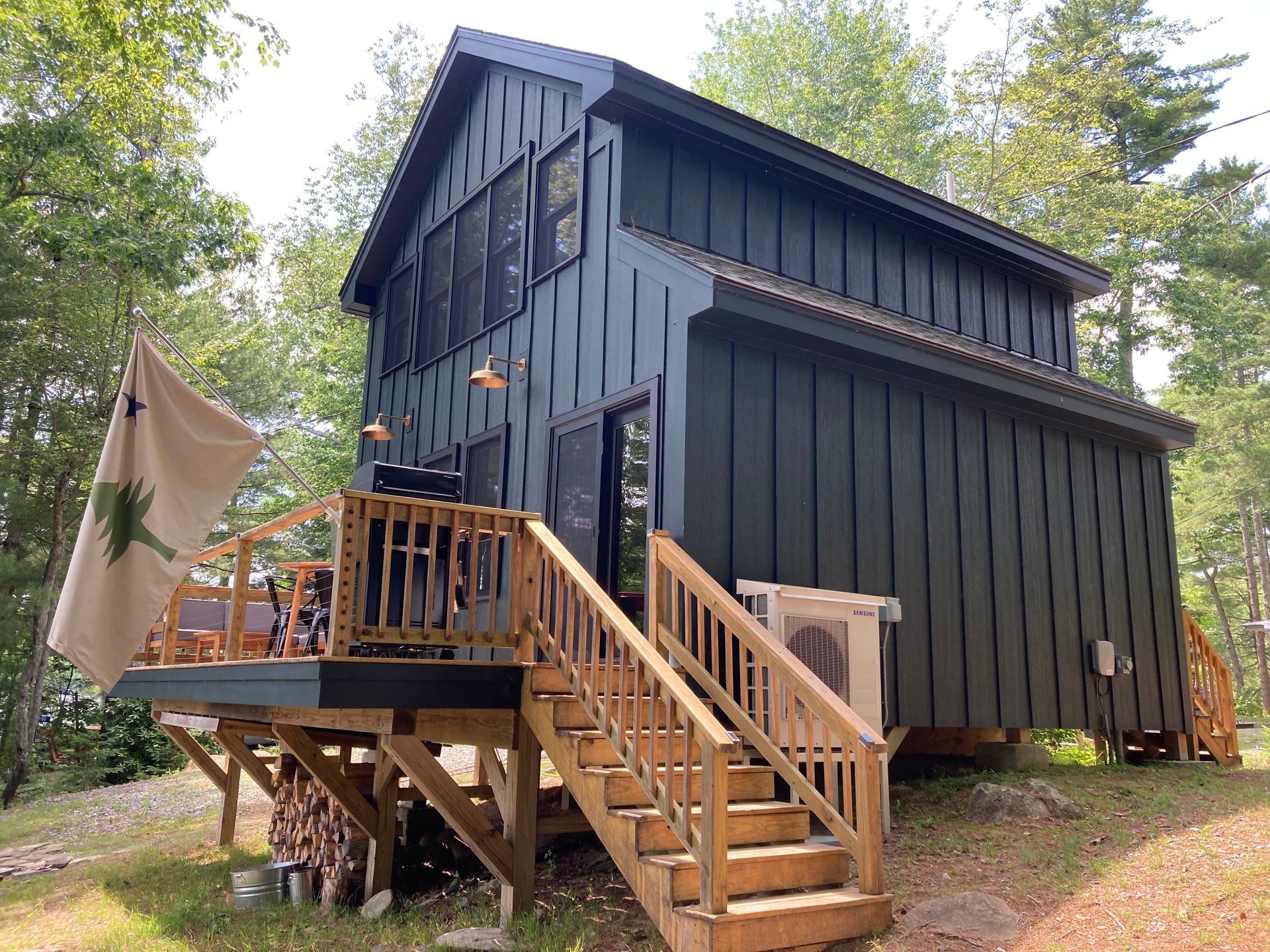 Dark gray cabin-style tiny house with wooden stairs and deck among trees outdoors