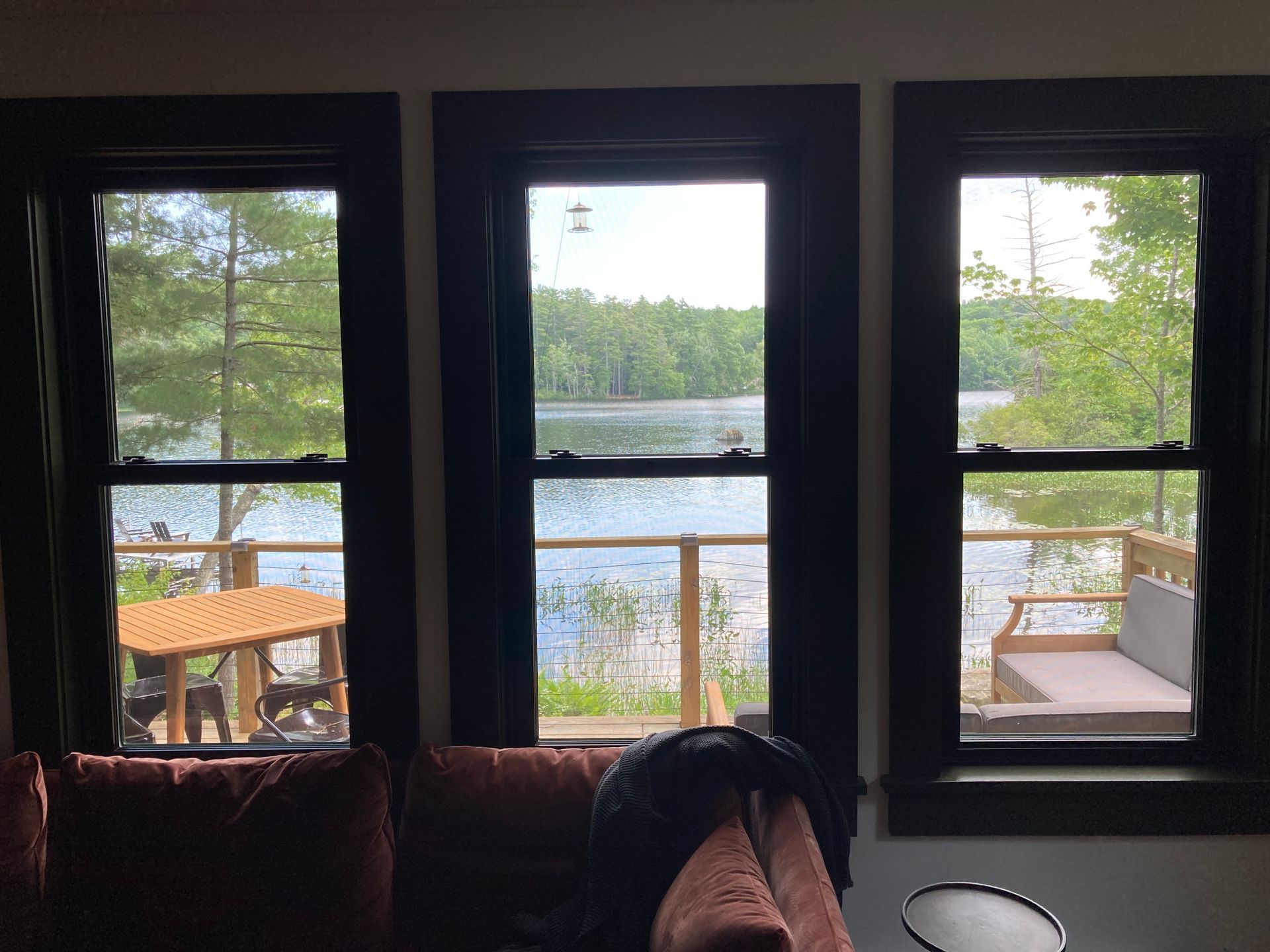 Three window panes overlooking a lake, dock, and trees, with a sofa in the foreground.