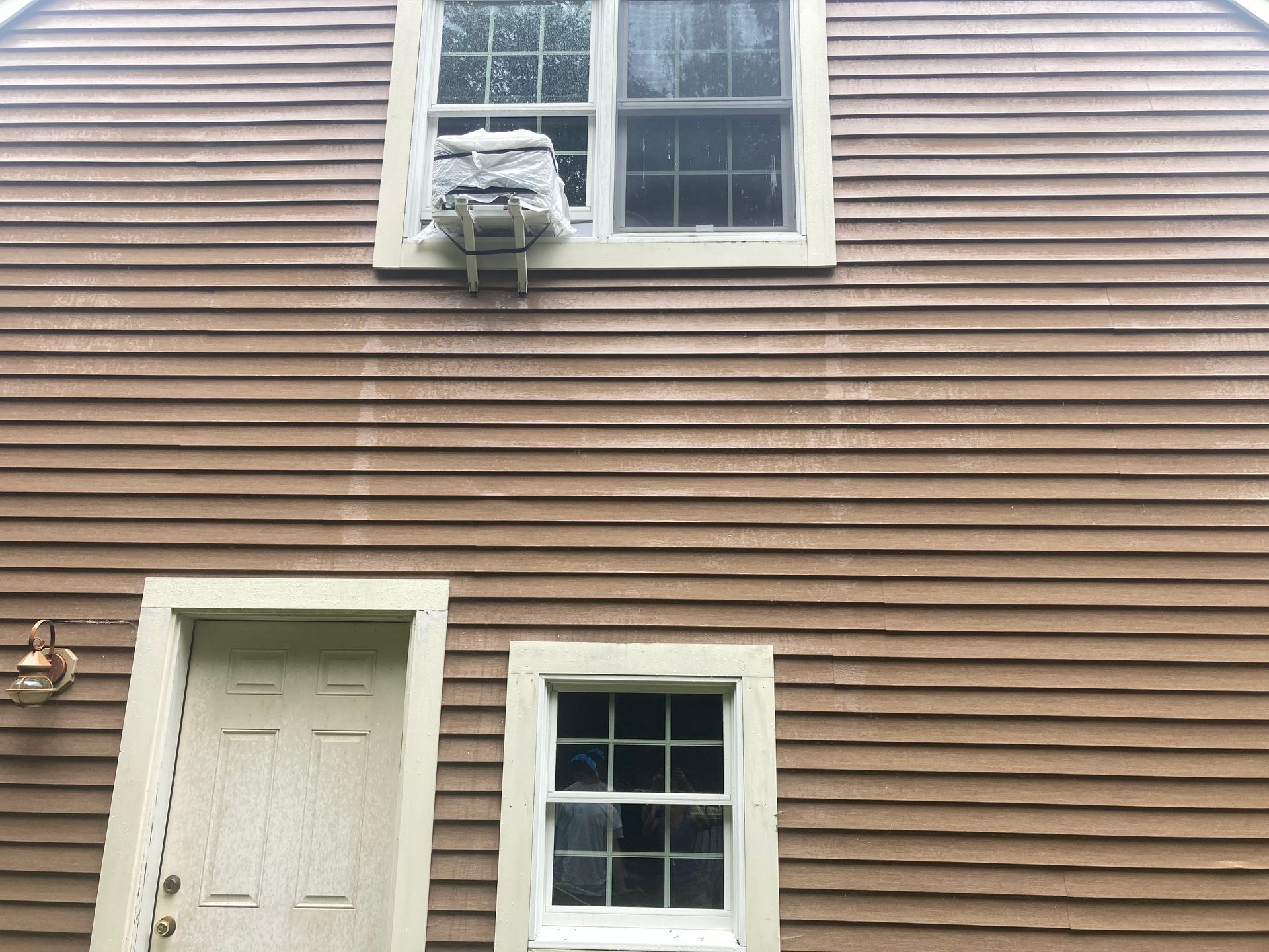 House exterior with tan siding, a white door, and two windows, one with a mounted air conditioner.