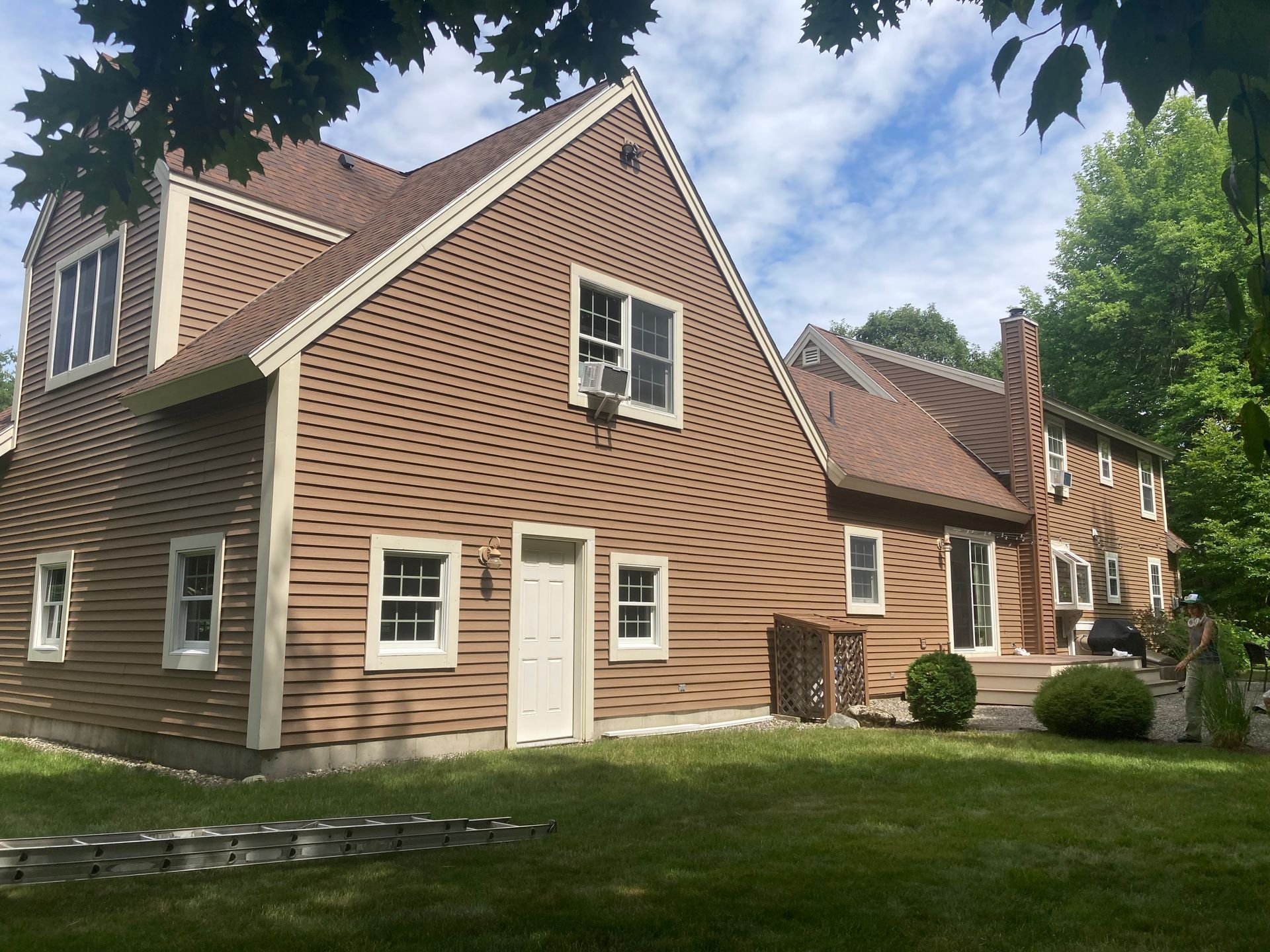 Brick house with white trim and steep roof, seen from the lawn under a partly cloudy sky.
