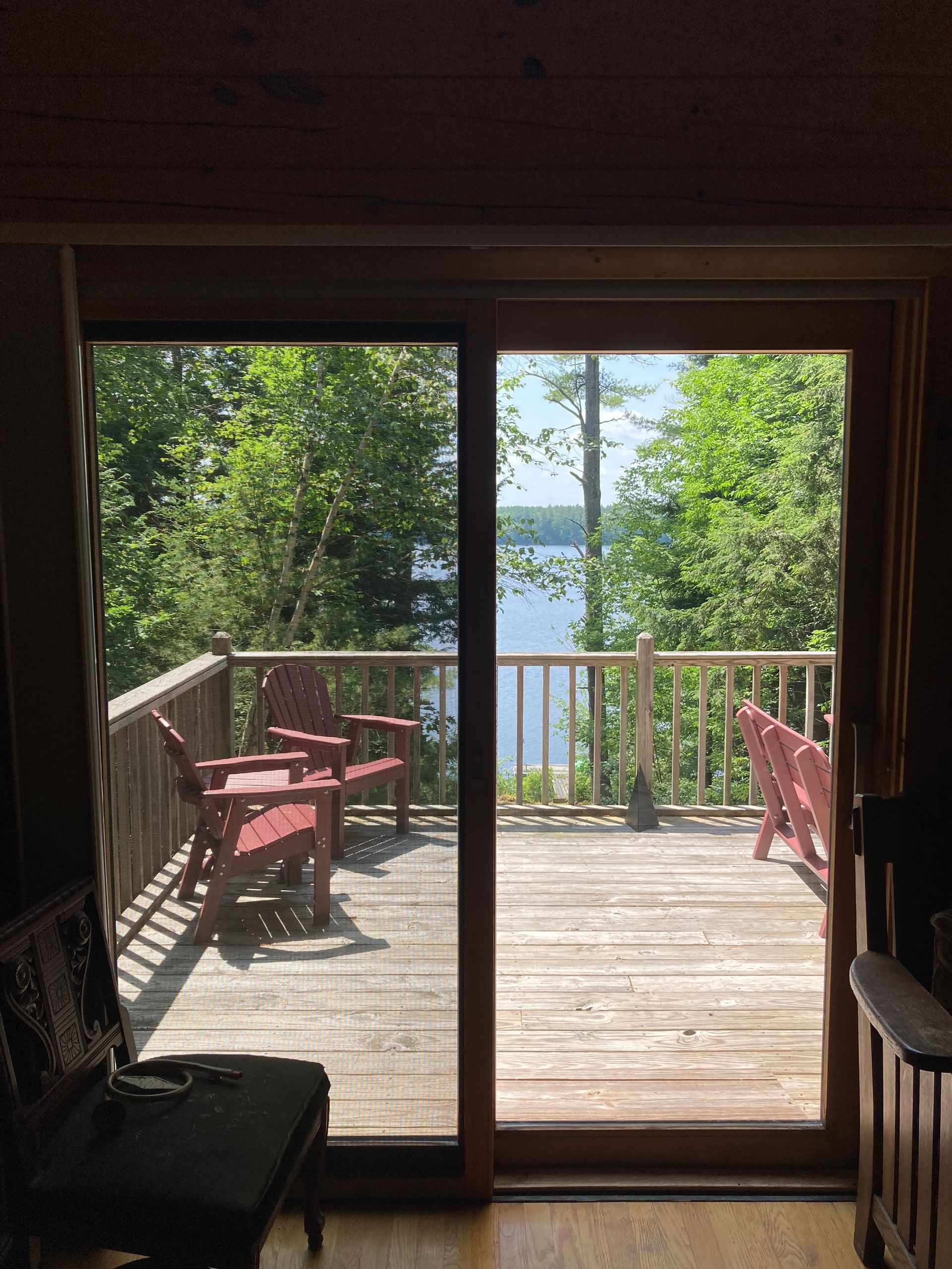 Wooden deck overlooking a lake through sliding glass doors, with red chairs and green trees outside