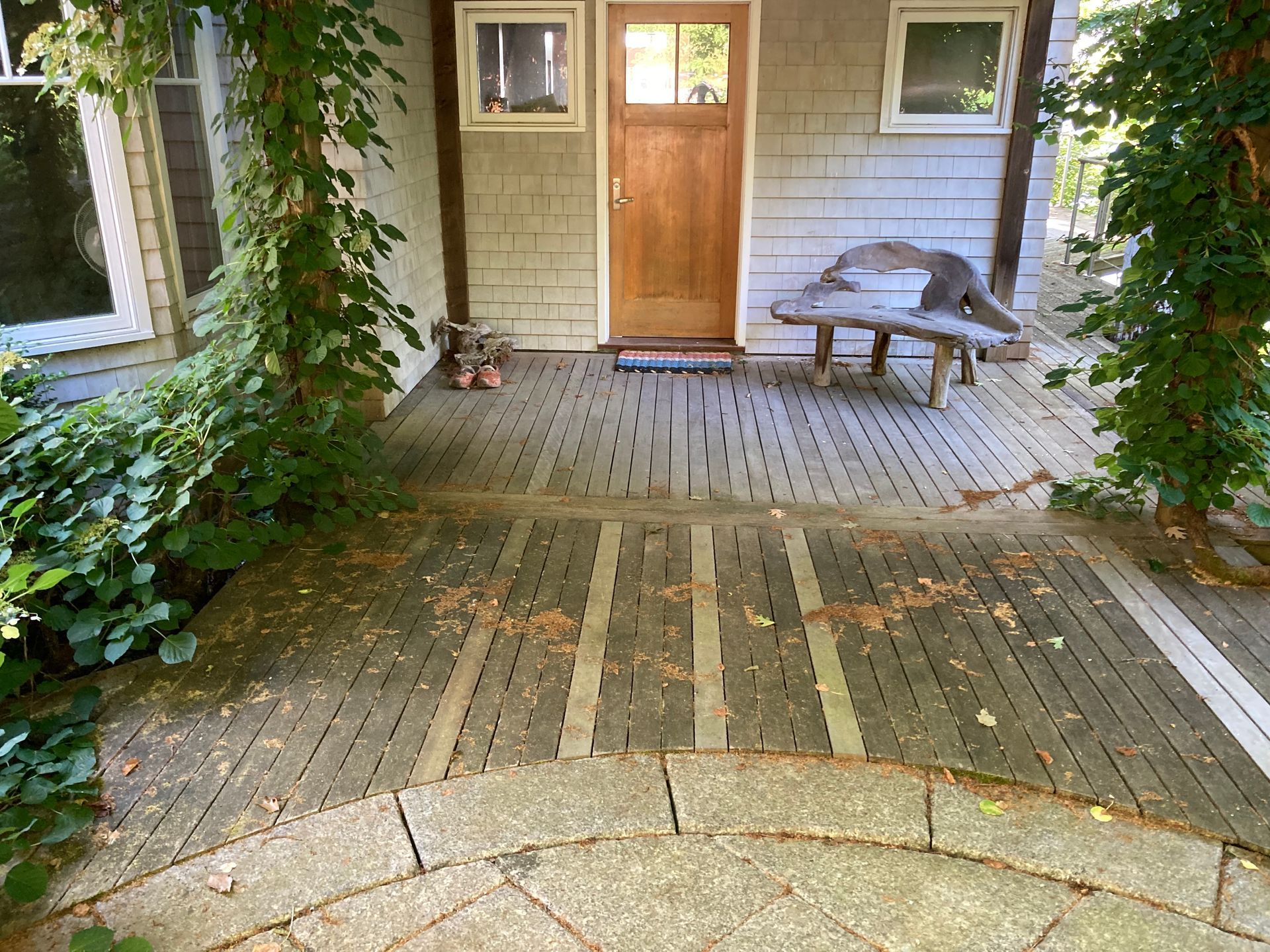 Front porch with a wooden door, bench, and ivy-covered brick walkway leading to the entrance