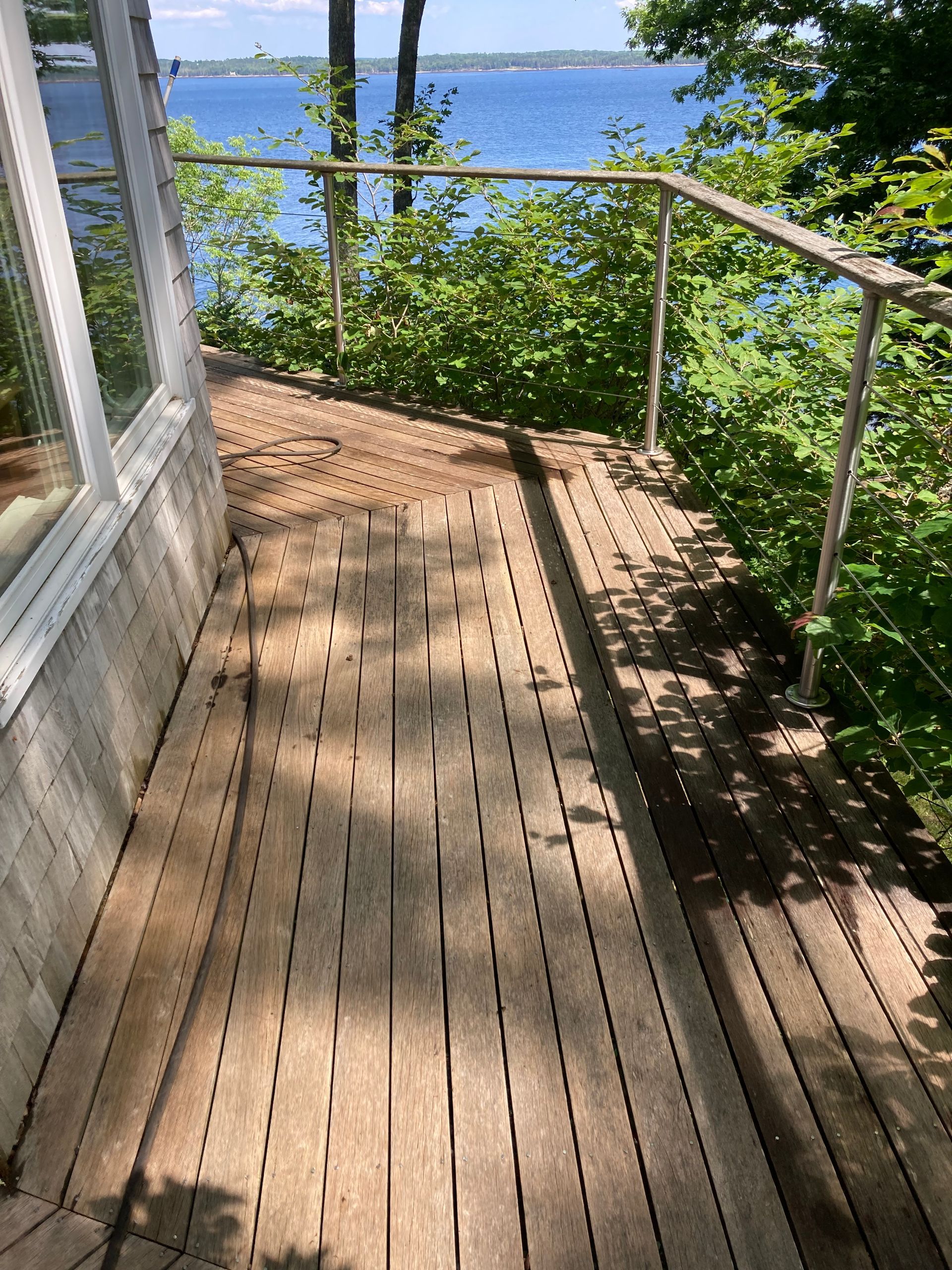 Wooden deck walkway with metal railing beside a lake and green trees on a sunny day