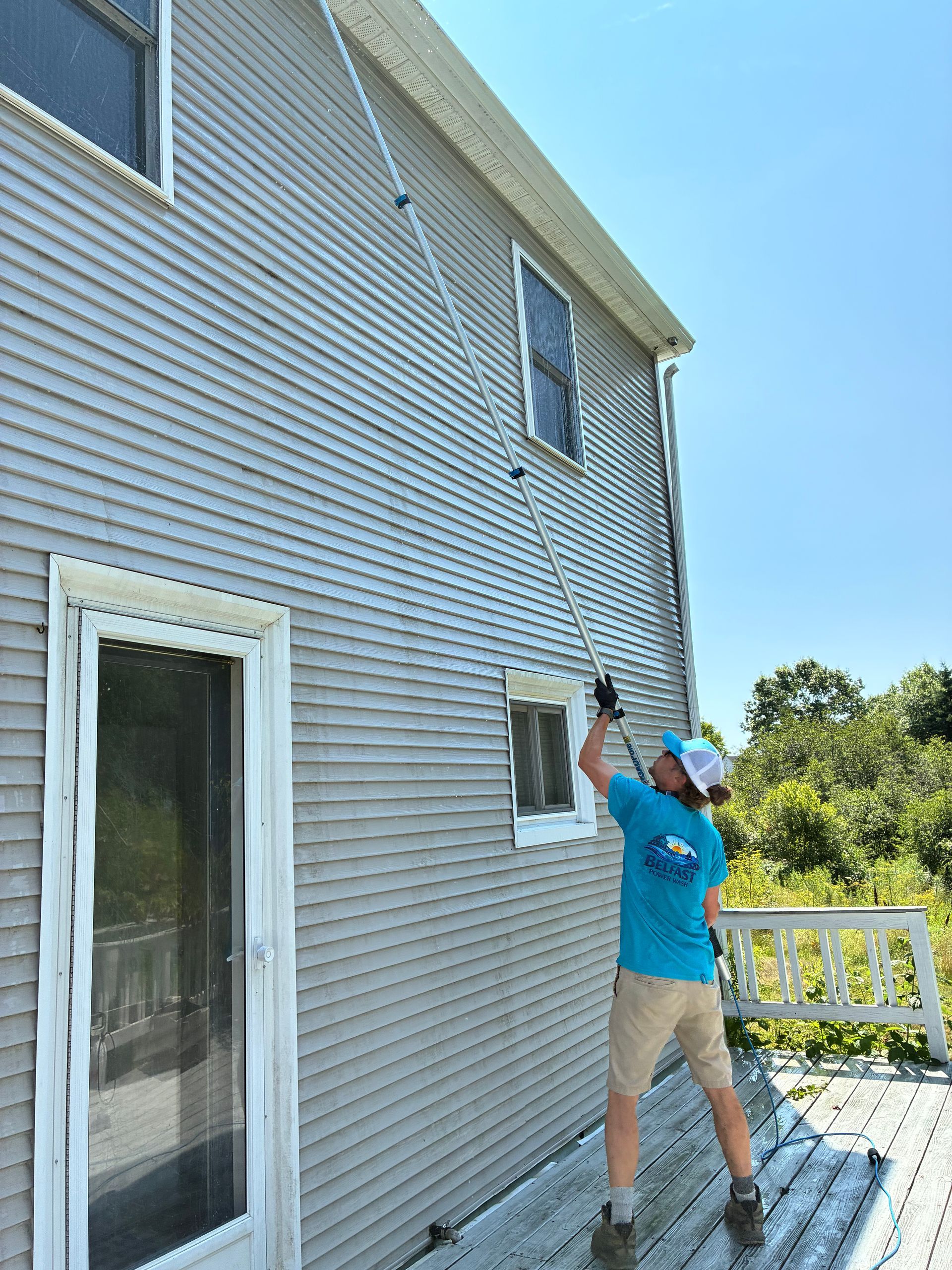 Person on a ladder washing second-story siding with a hose on the side of a house.